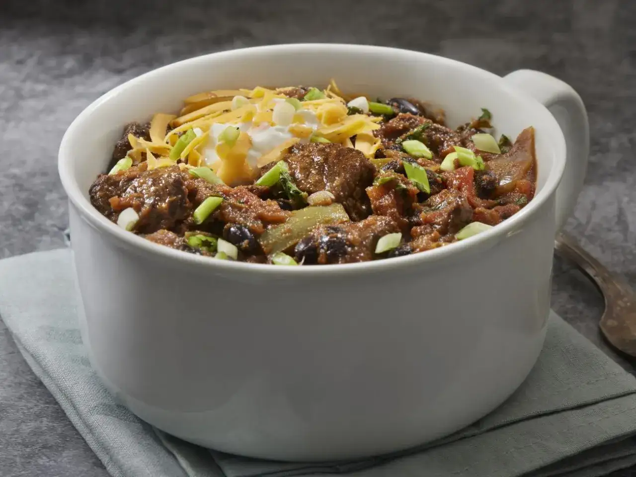 Gęste, aromatyczne dania na imprezę na ciepło: chili con carne z wołowiną, fasolą, pomidorami, posypane serem i szczypiorkiem.