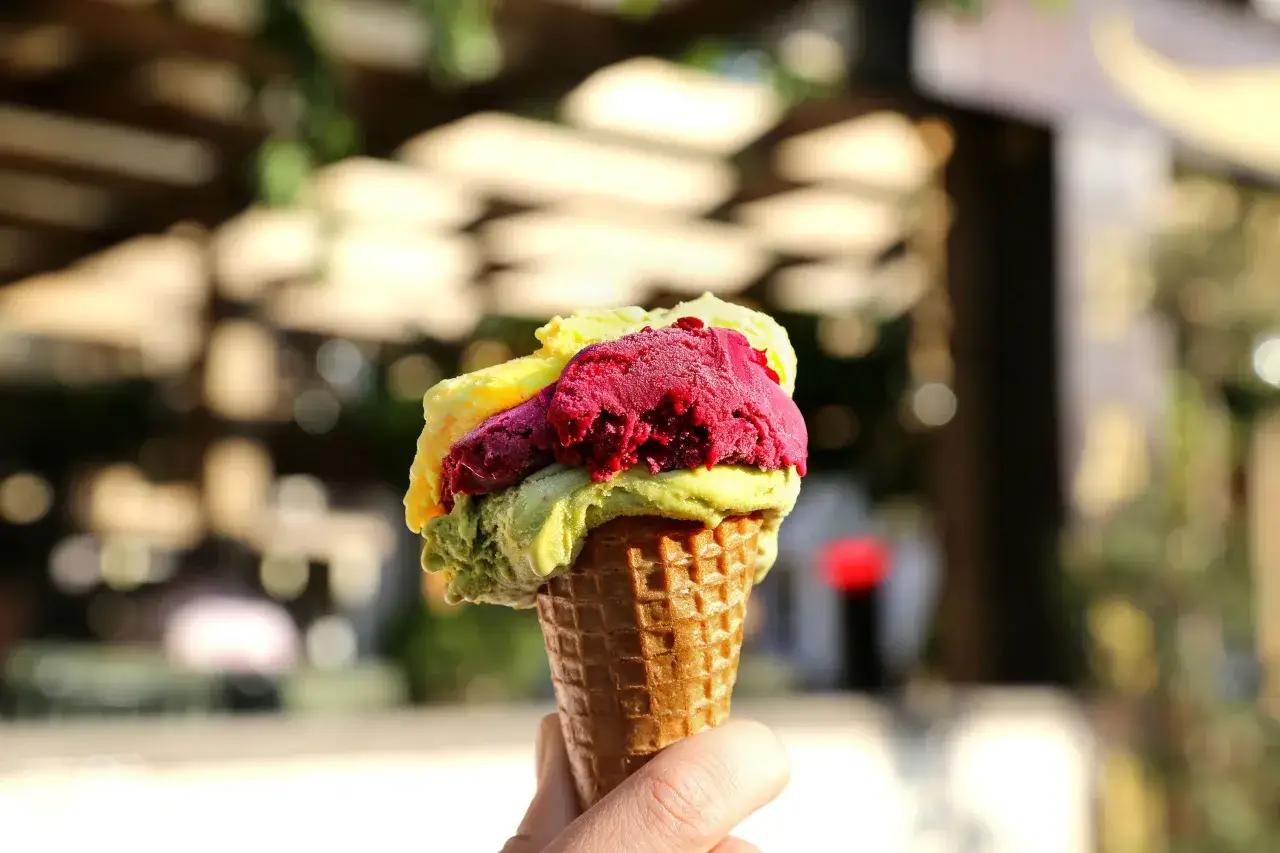 Hand hält eine Waffel mit drei Kugeln Eis: grün, rot und gelb. Ein Genuss, der wie das beste Eis der Welt schmeckt!