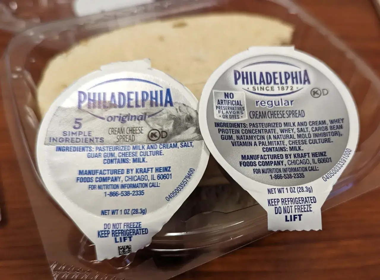 Zwei kleine Becher Philadelphia Cream Cheese Spread, original und regular, in einer Plastikverpackung.