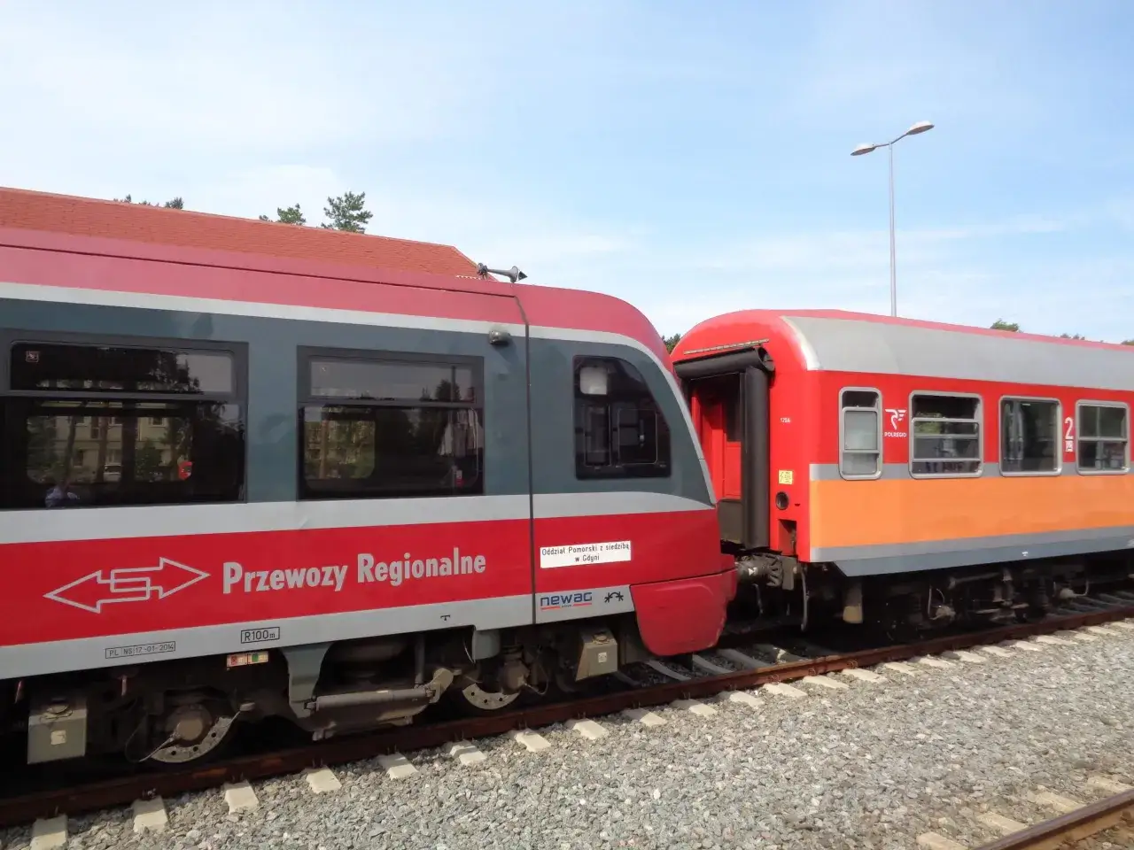 Dwa pociągi stojące na torach. Jeden czerwono-szary z napisem