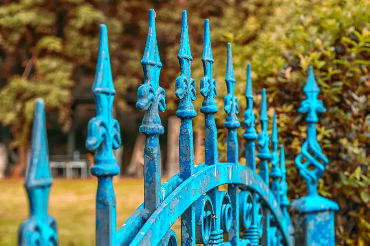 Cancello in ferro battuto blu, con punte aguzze e decorazioni a spirale, mostra segni di usura, suggerendo un recente lavoro di verniciare cancello a spruzzo per rinnovarlo.