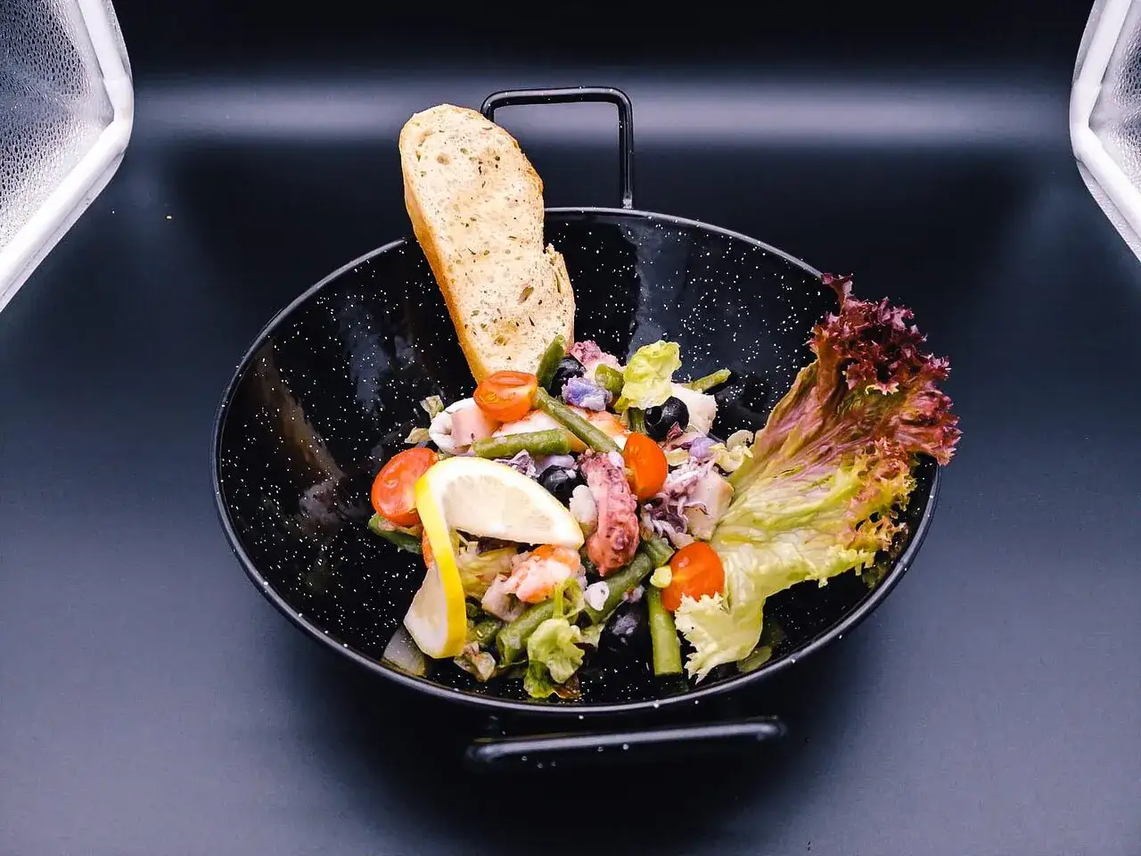 Ein bunter Salat mit Fisch, Garnelen und Tintenfischringen, garniert mit Zitrone, Tomaten, Oliven und Brot.