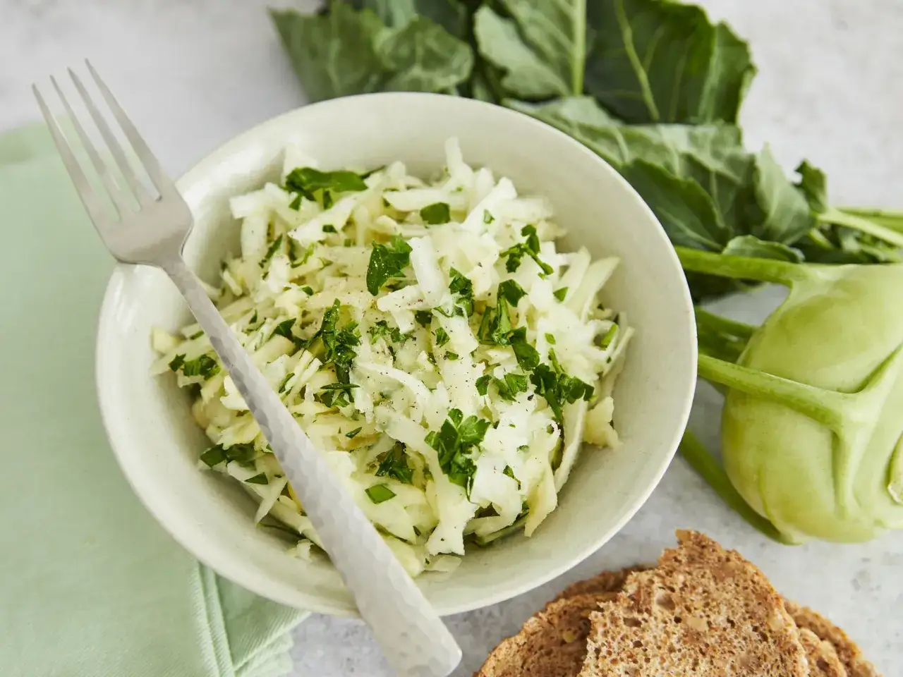 Frischer Kohlrabi Salat mit Petersilie, daneben ein Kohlrabi und Brot.