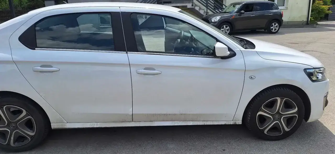 Biały Citroen C Elysée lekko zabrudzony, zaparkowany na zewnątrz.