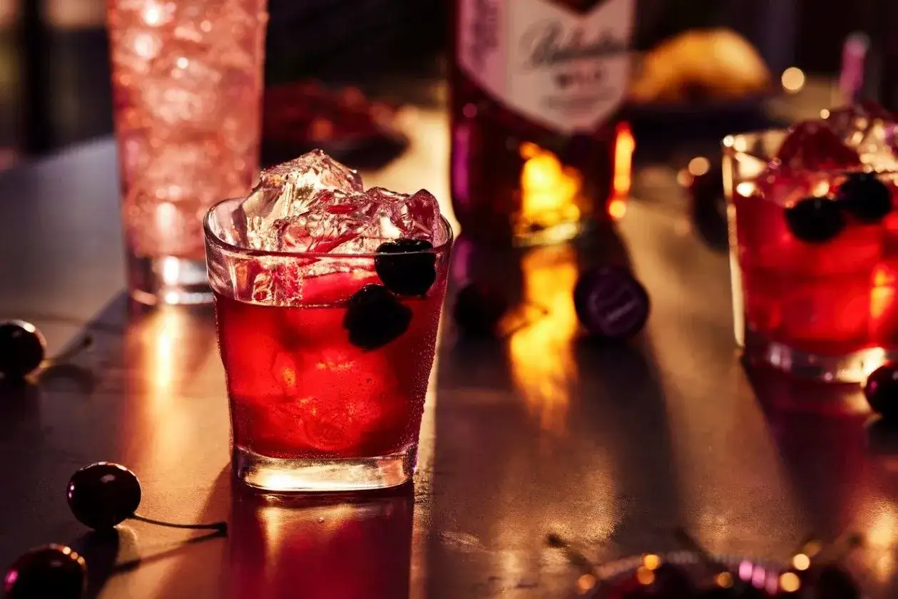 Ballantines Wild z czym pić? Czerwony koktajl z wiśniami i lodem, obok butelka Ballantines Wild.