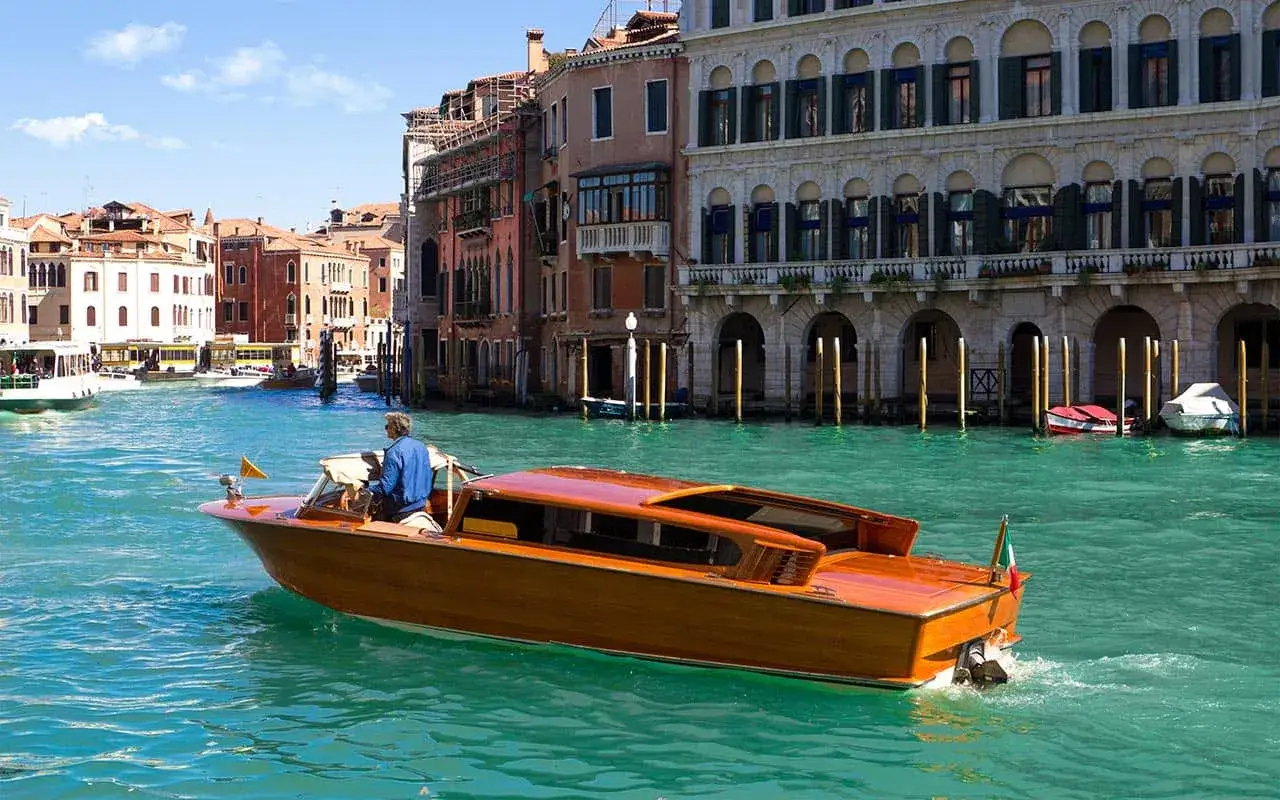 Un elegante taxi boat in legno naviga sul Canal Grande a Venezia, con palazzi storici sullo sfondo.