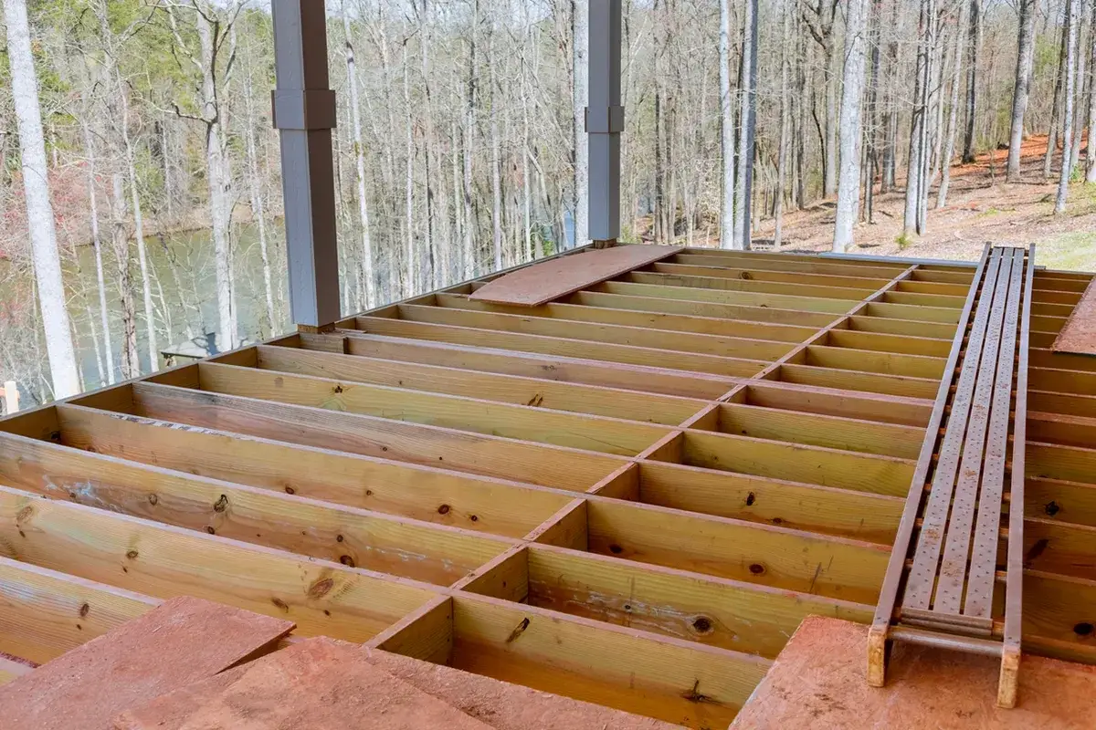 Construction d'un plancher d'étage : le solivage en bois est posé, prêt pour les lames. Vue sur la forêt et un lac.