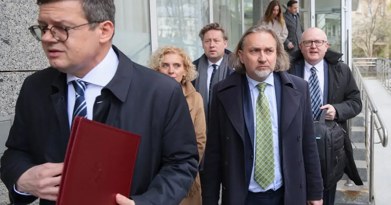 Grupa osób w eleganckich strojach, prawdopodobnie skład trybunału konstytucyjnego, wychodzi z budynku.