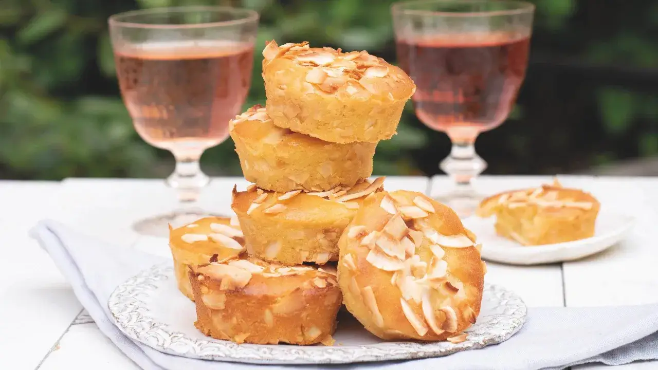 Sm&aring;, gyllene muffins med mandelflagor, perfekta att baka med citron. Tv&aring; glas ros&eacute; i bakgrunden.