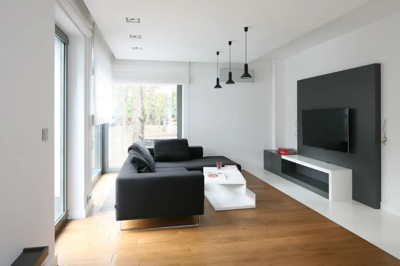 Nowoczesny salon z ciemnoszarą kanapą, białym stolikiem i drewnianą podłogą. Idealne miejsce, by zastanowić się, jakie panele do białych ścian będą pasować.
