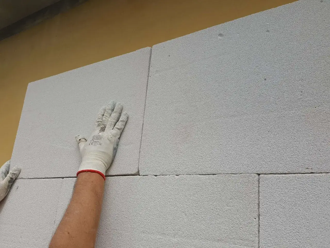 Mano guantata posiziona blocchi leggeri per un cappotto termico. La scelta giusta è fondamentale per l'isolamento.