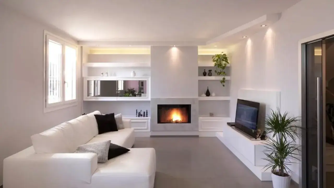 Soggiorno moderno con camino a gas e libreria in cartongesso integrata, divano bianco e TV.