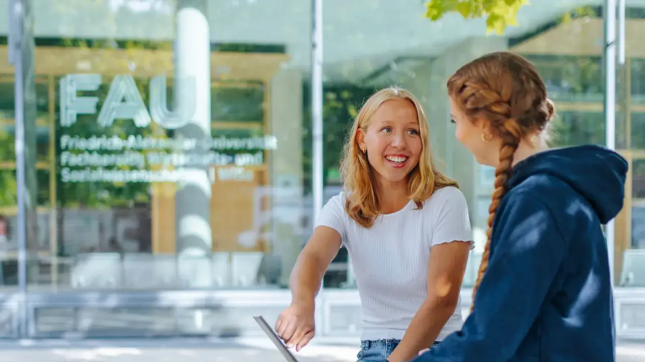 Zwei Studentinnen lachen vor der FAU. Perfekt für die Werbung für ein Studium an der Friedrich-Alexander-Universität.