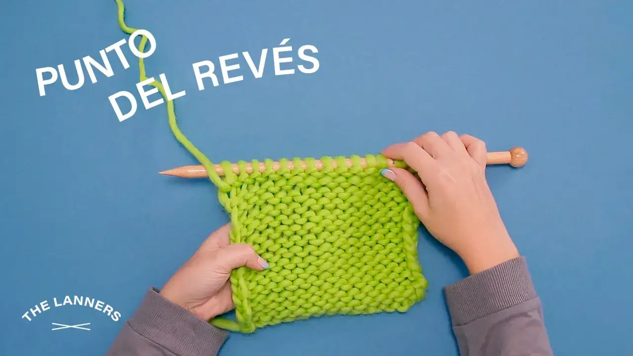 Manos tejiendo con agujas de madera un punto jersey revés de lana verde brillante.