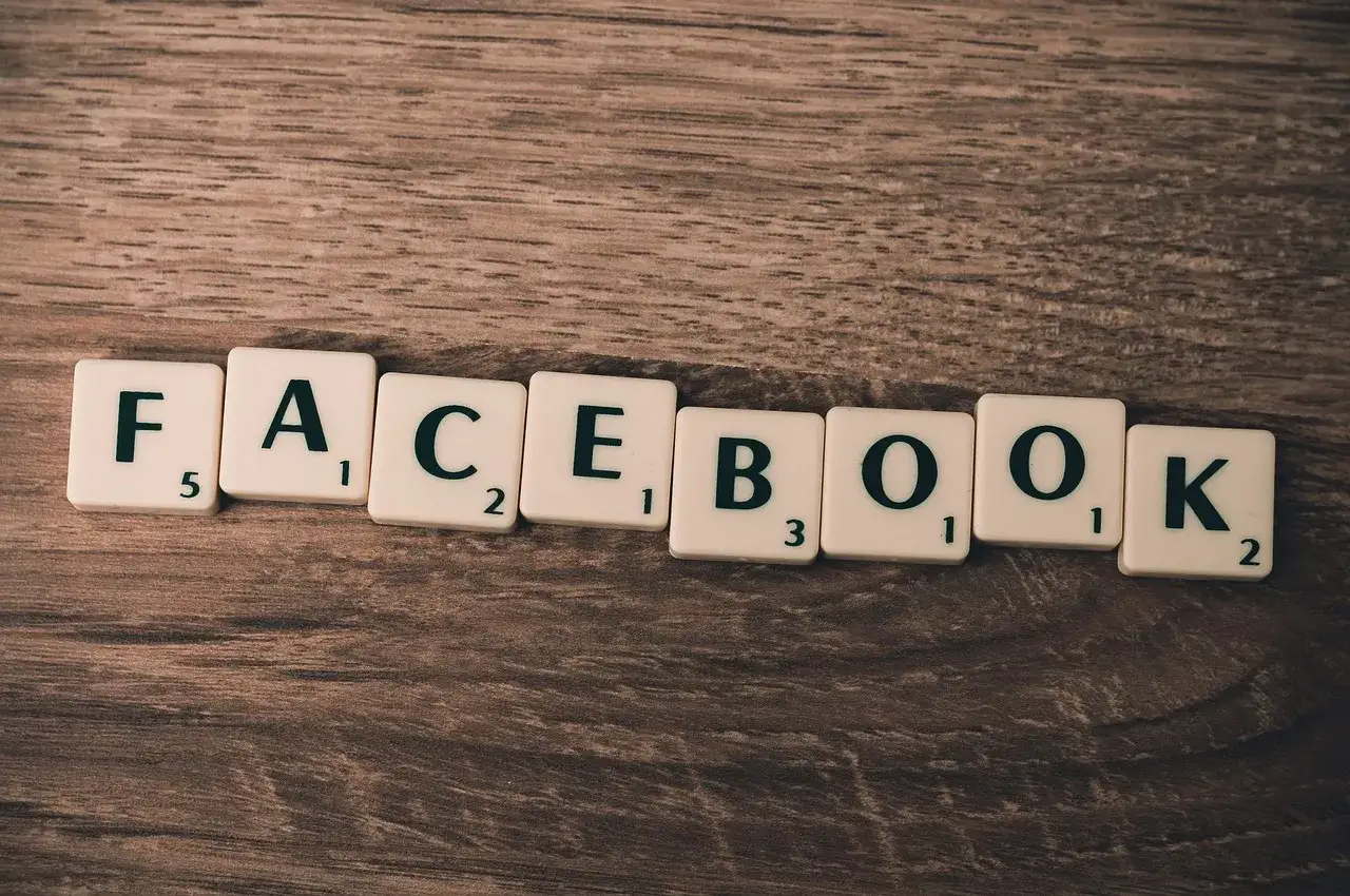 Litery na drewnianym tle układają słowo FACEBOOK. Chcesz wiedzieć, jak zmienić numer tel na FB?