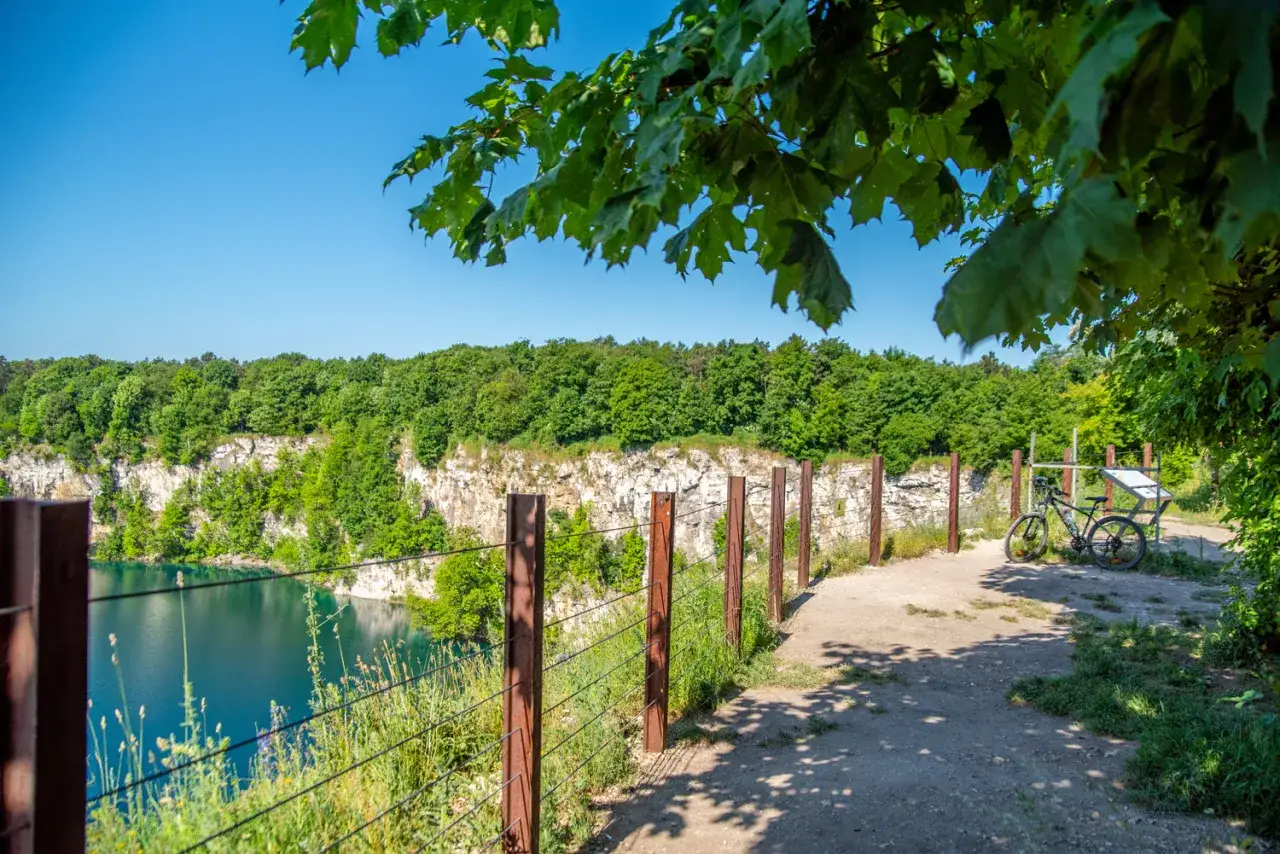 Kraków, jezioro Zakrzówek. Ścieżka z rowerem prowadzi nad turkusową wodą, otoczoną skalnymi klifami i zielonym lasem.