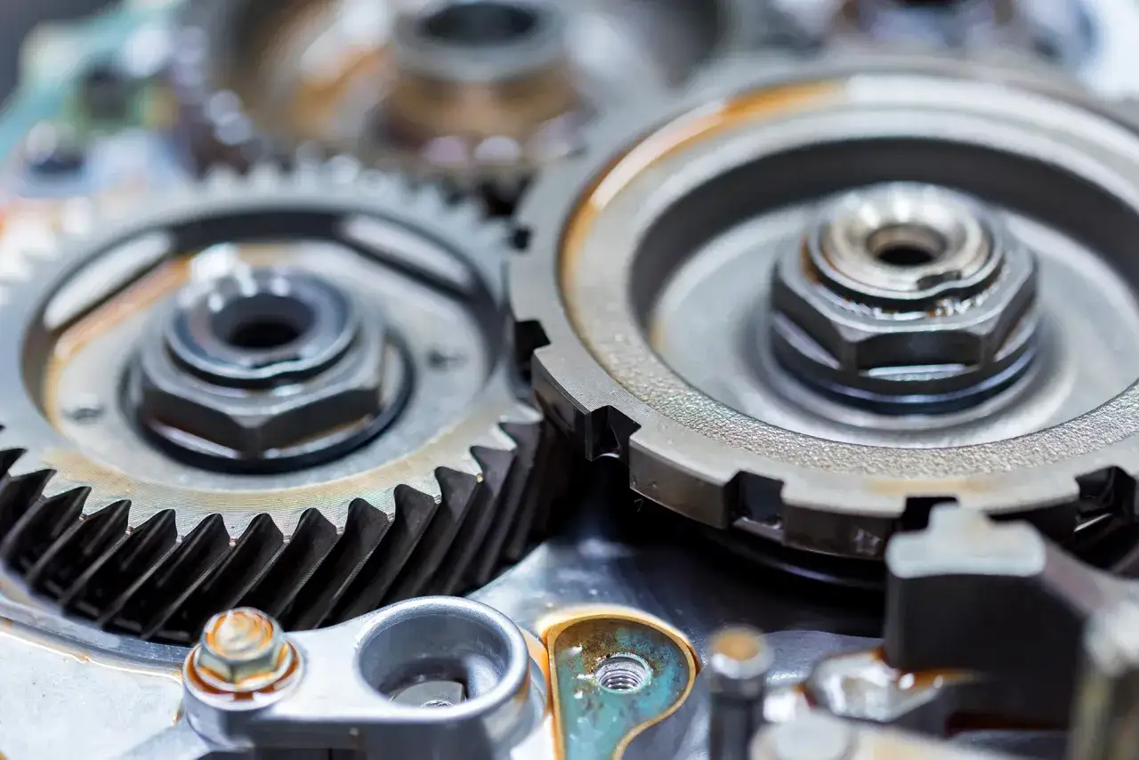 Zbliżenie na mechanizm skrzyni biegów, widoczne zębatki i śruby. Może to być element luźny drążek zmiany biegów, wymagający naprawy.