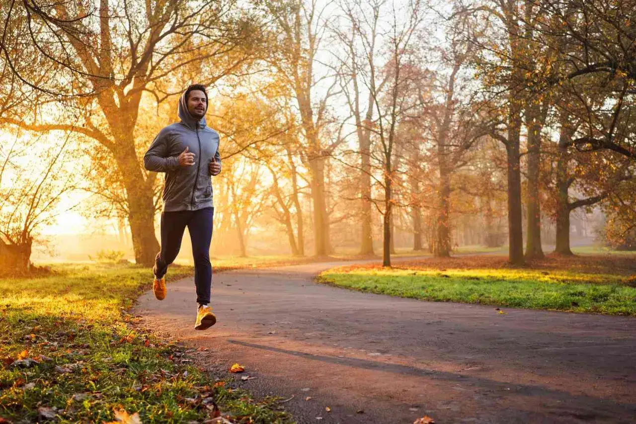 Uomo corre in un parco autunnale al tramonto. Per capire quanti km correre al giorno per dimagrire, &egrave; fondamentale un piano personalizzato.