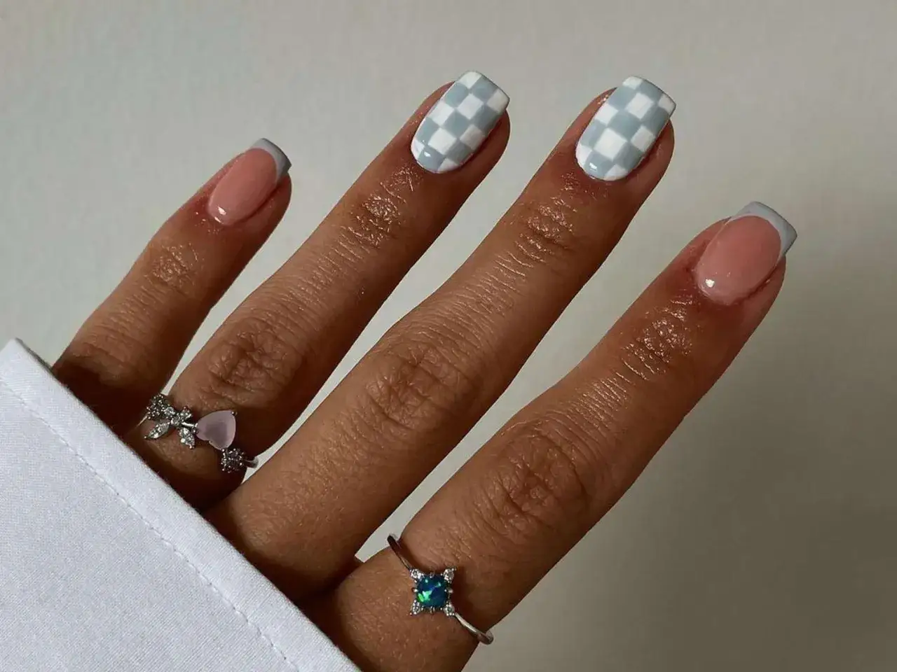 Fingrar med fransk manikyr och rutiga naglar i ljusbl&aring;tt och vitt. Ett gr&aring;tt nagellack ger en sofistikerad touch.