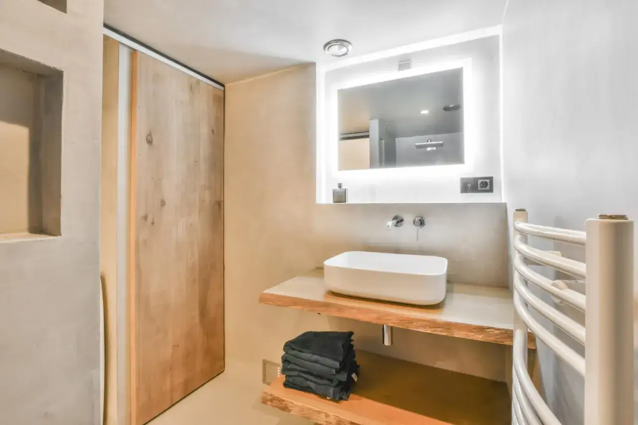 Modernos **ba&ntilde;os peque&ntilde;os** con lavabo sobre encimera de madera, espejo iluminado y puerta corredera de madera.