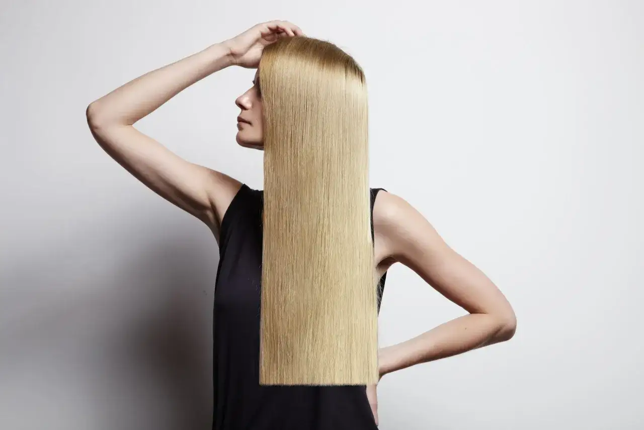 Donna con lunghi capelli biondi lisci, che mostra come lisciare i capelli a casa con facilità.