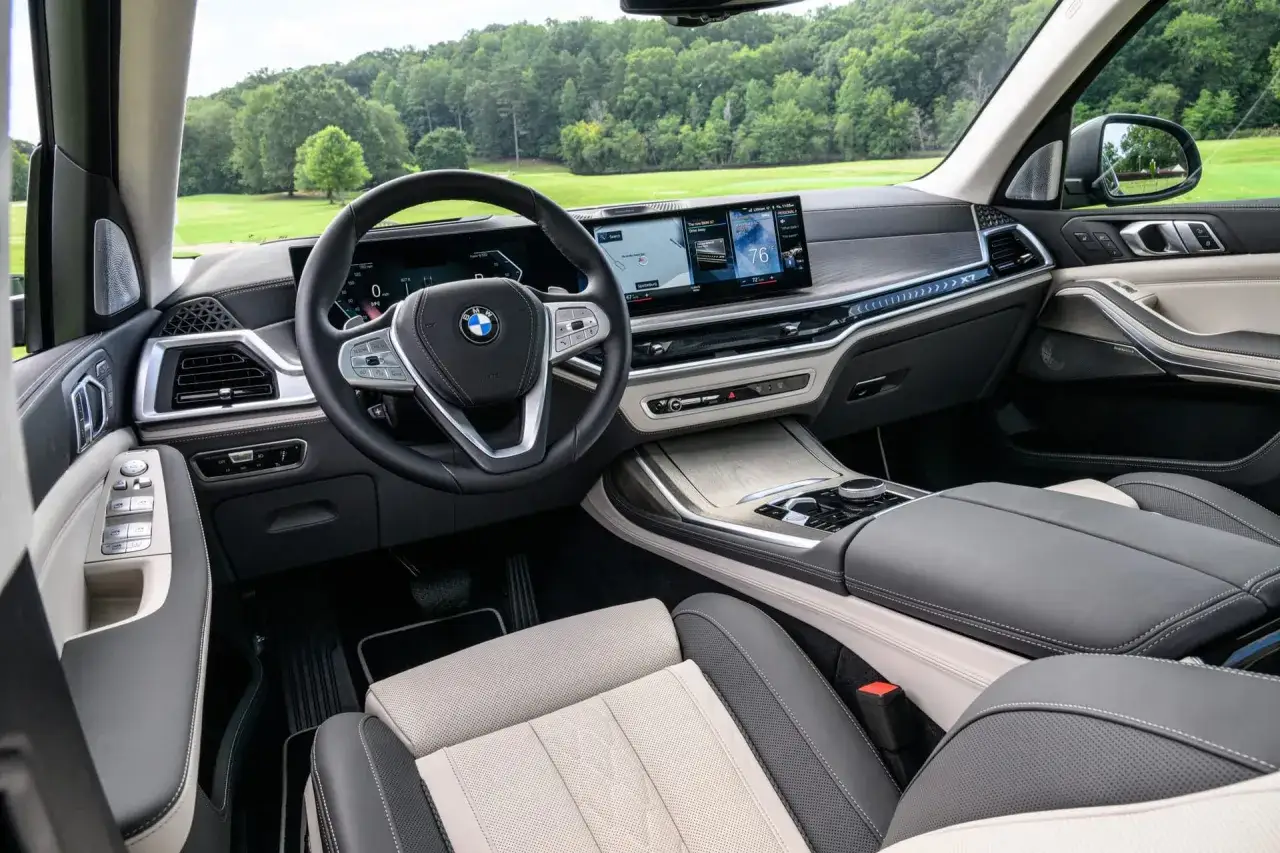 Wnętrze BMW X7 2025 z dwukolorową tapicerką, nowoczesnym kokpitem i widokiem na zielone wzgórza.