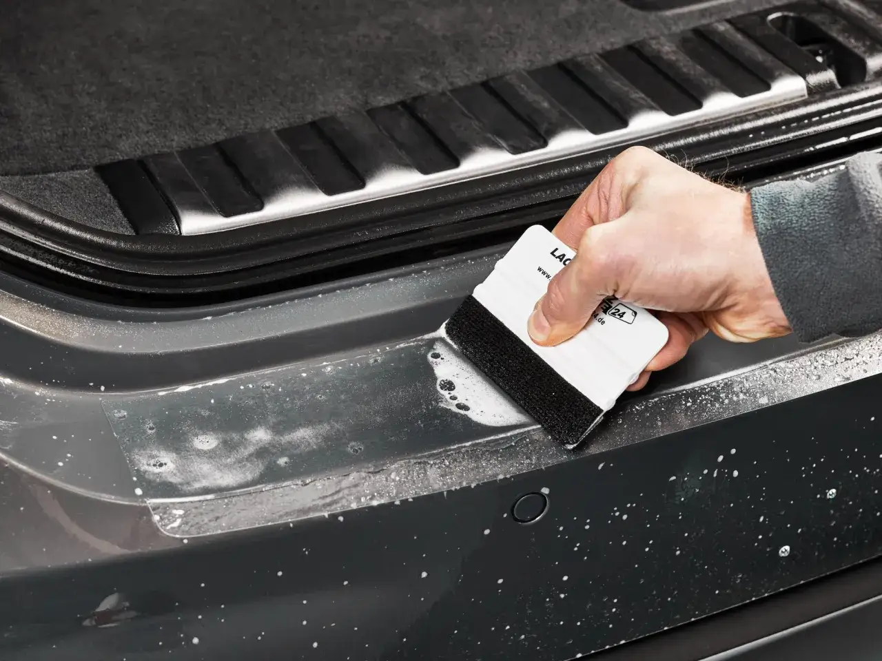Mit der Rakeltechnik Anleitung wird die Folie blasenfrei angebracht. Ein wei&szlig;er Rakel mit schwarzem Filzrand gleitet &uuml;ber die nasse Oberfl&auml;che des Autos.