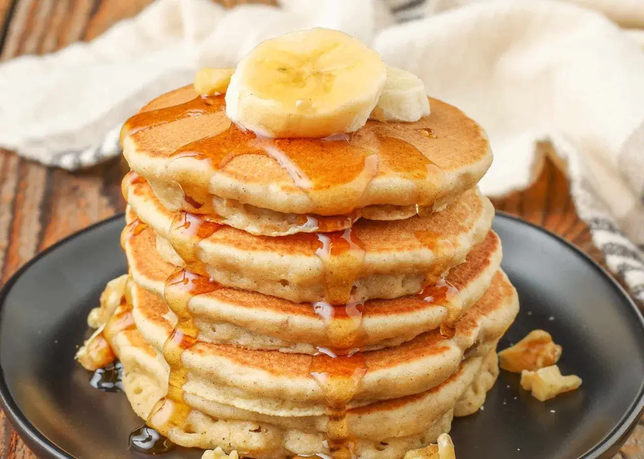 Ein Stapel fluffiger Bananenpfannkuchen, beträufelt mit Sirup und garniert mit Bananenscheiben.