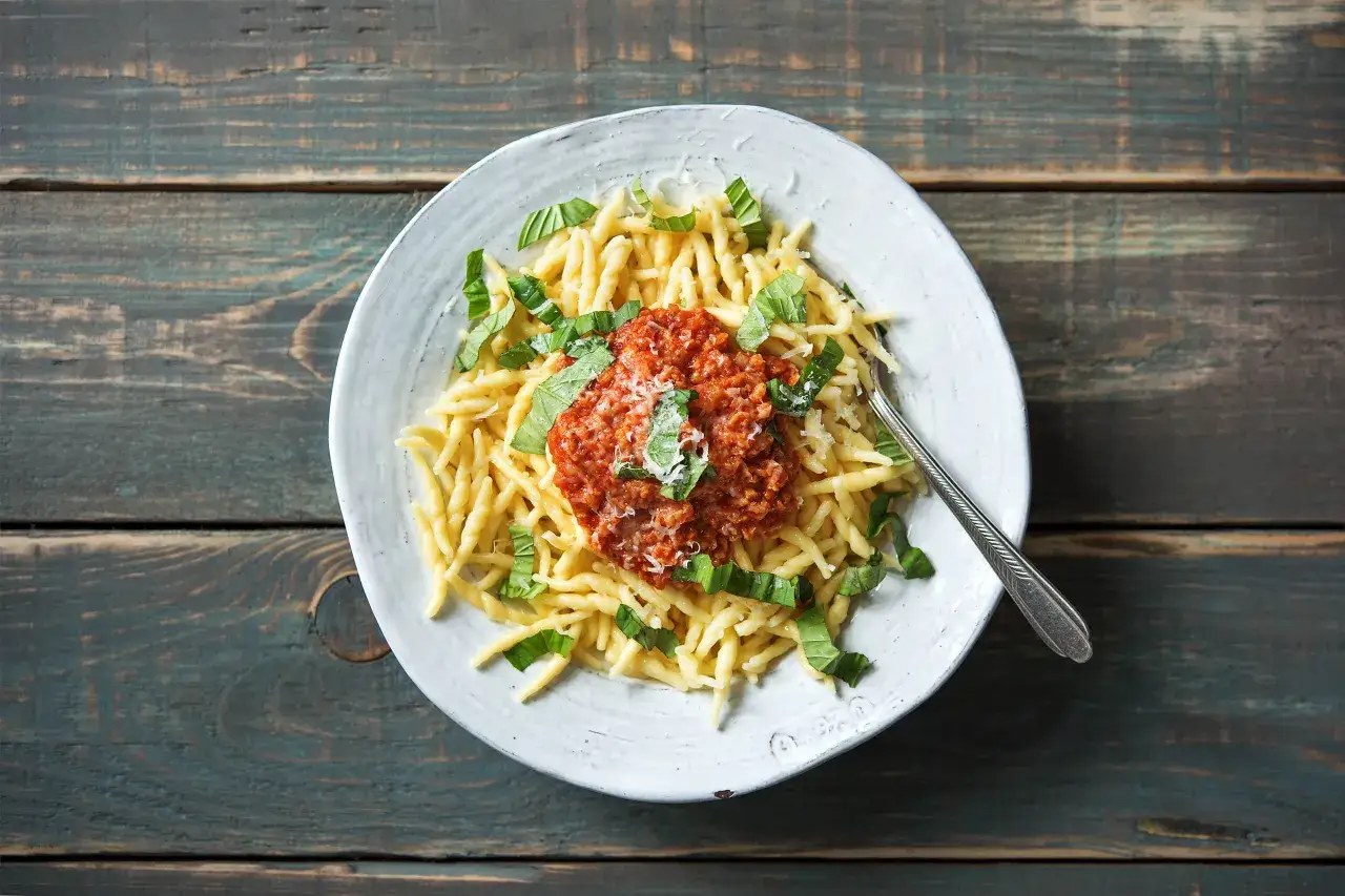 Herzhafte vegetarische Bolognese mit frischem Basilikum und Parmesan auf gedrehten Nudeln, serviert auf einem rustikalen Holztisch.