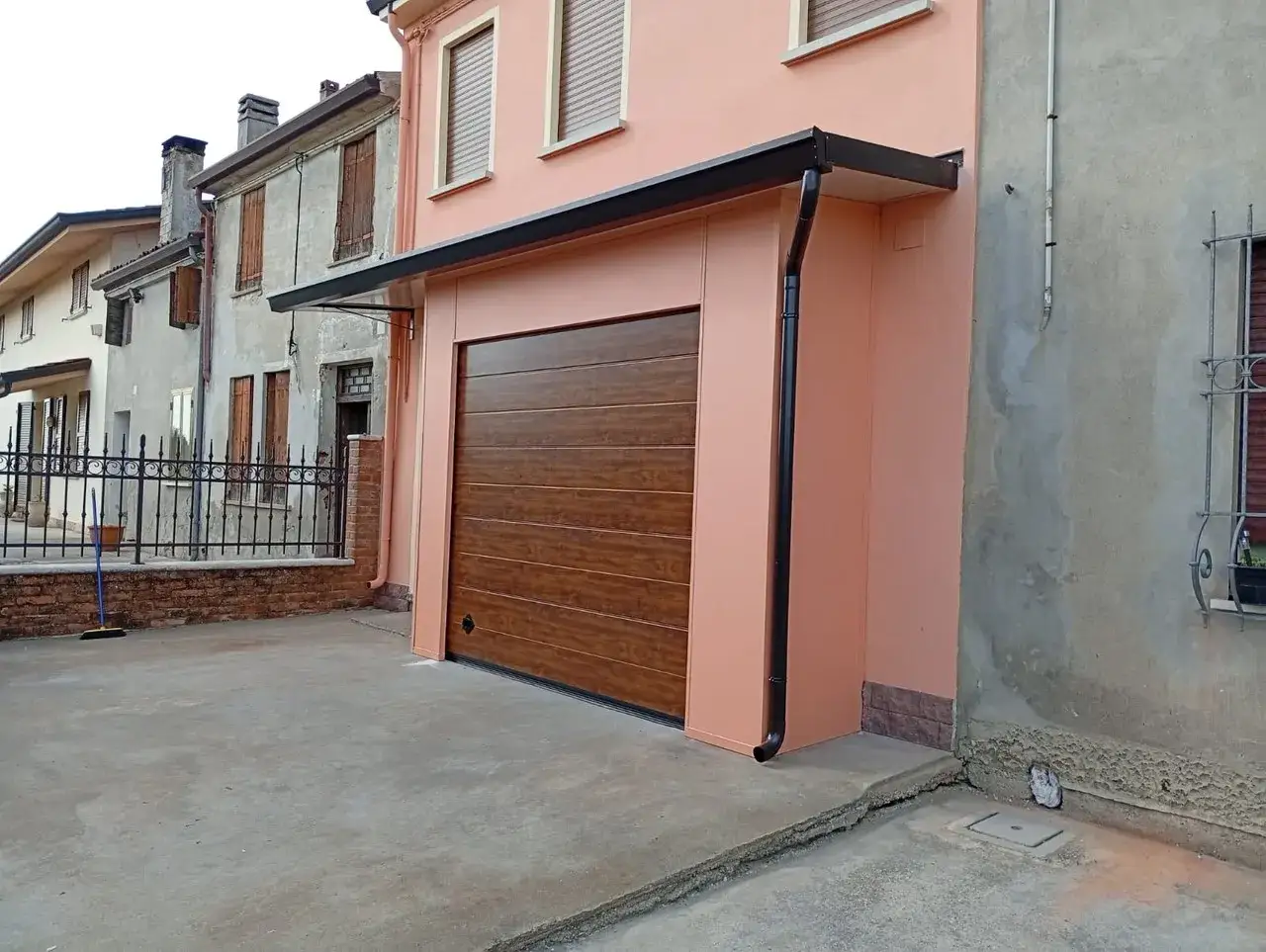 Un nuovo garage con portone sezionale in legno offre ampio spazio di manovra per il passo carrabile.