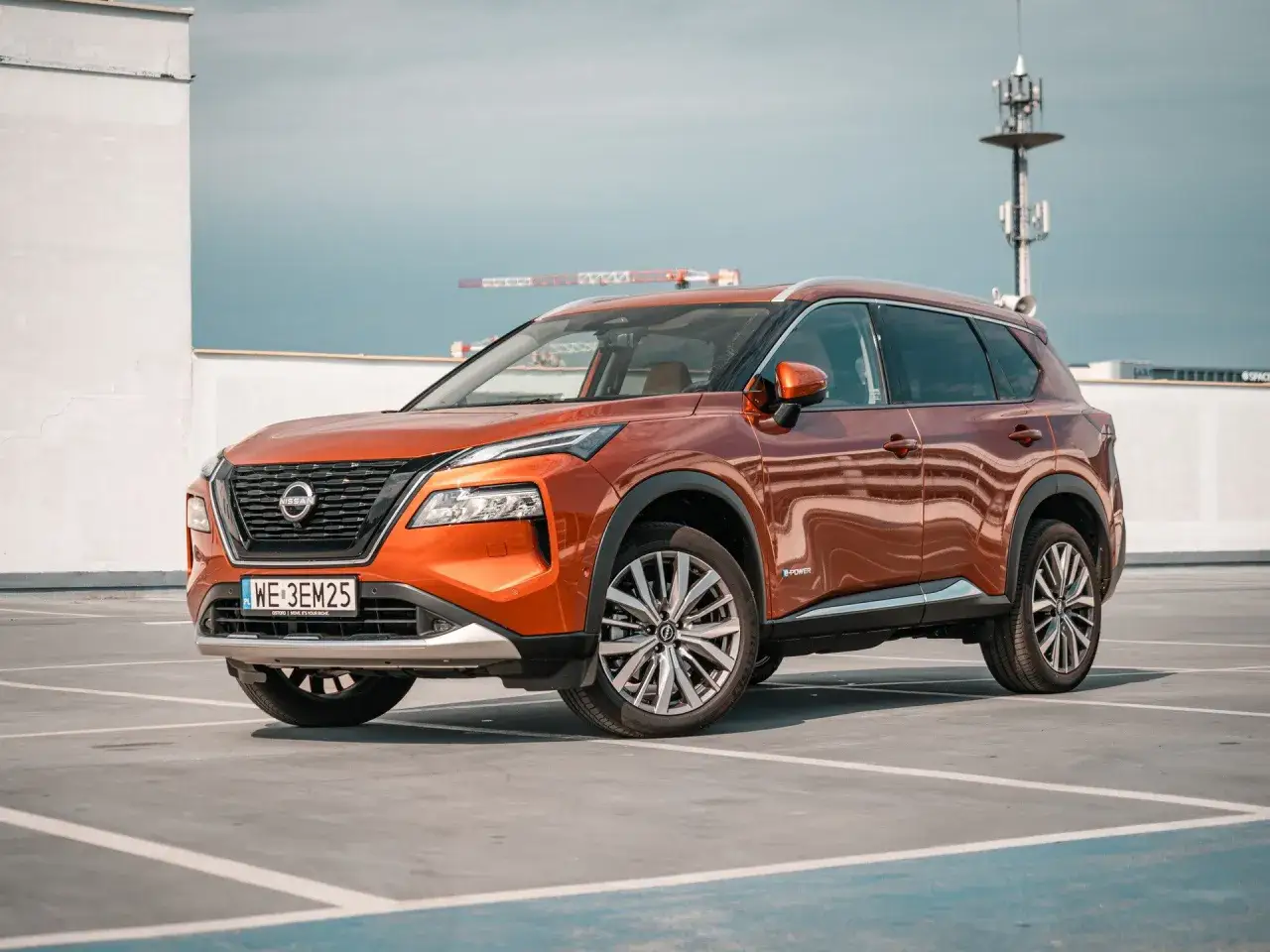 Pomarańczowy Nissan X-Trail e-POWER na parkingu. Zastanawiasz się, jaki silnik wybrać? Ten model oferuje innowacyjne rozwiązanie hybrydowe.