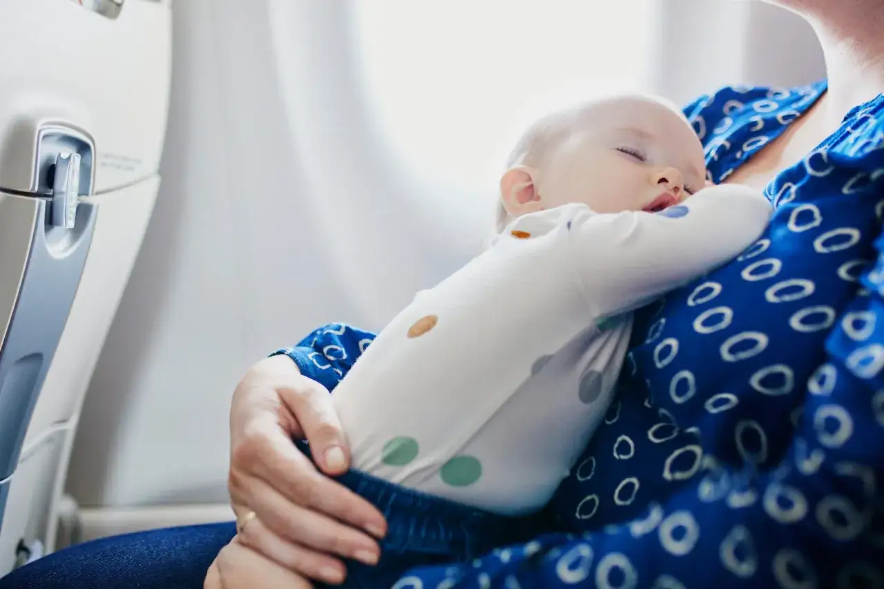 Śpiące dziecko na rękach mamy w samolocie. To bagaż dla niemowlaka, który podróżuje z rodzicami.
