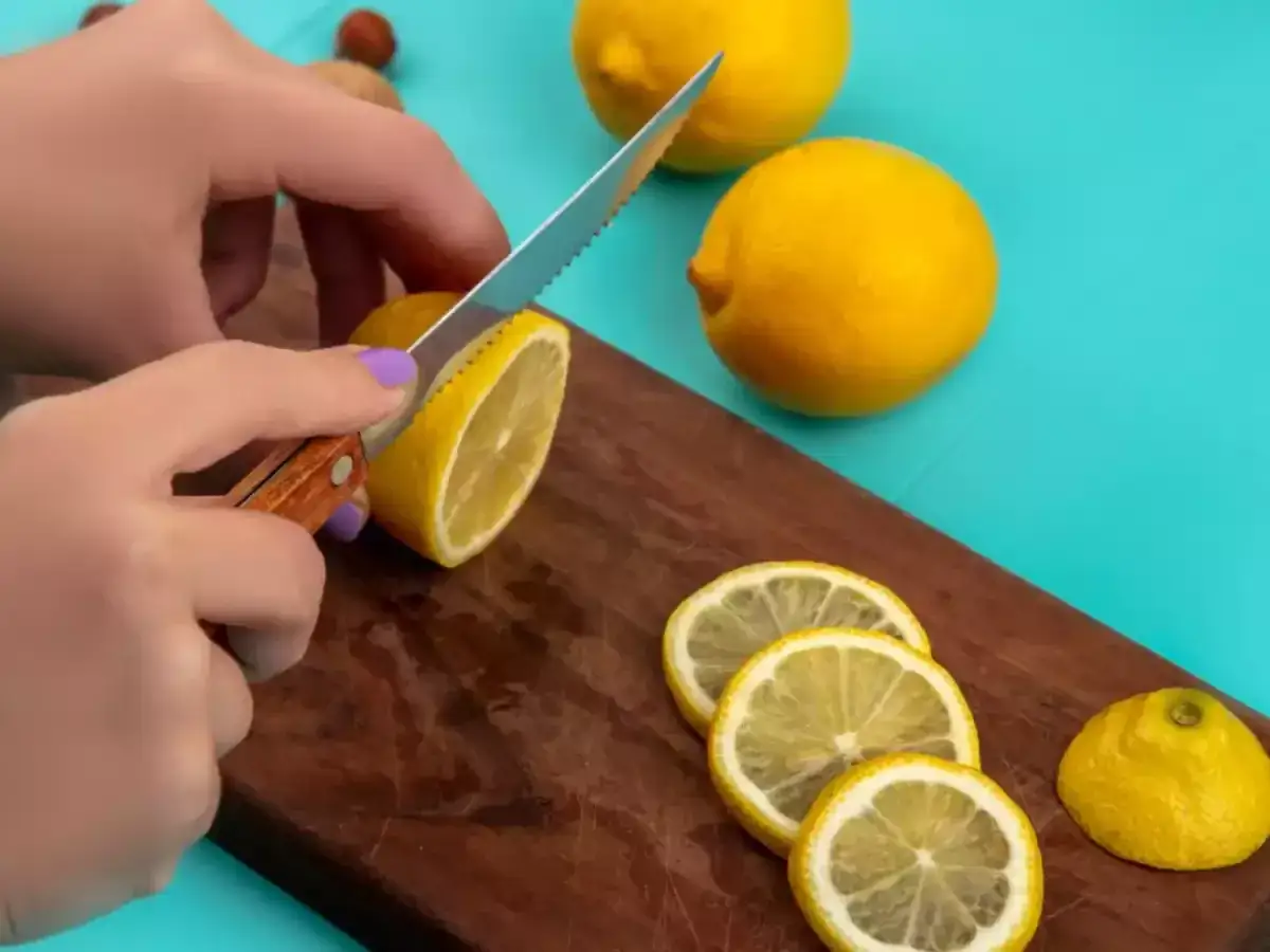 Hände schneiden eine Zitrone in Scheiben. So kann man Zitronen einfrieren und immer frisches Aroma zur Hand haben.