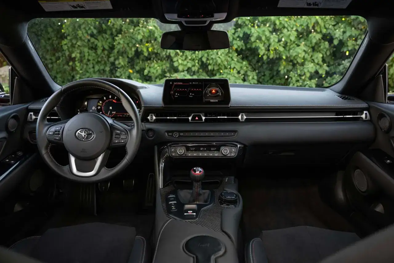 Interior del Toyota Supra, con volante deportivo, pantalla digital y palanca de cambios.