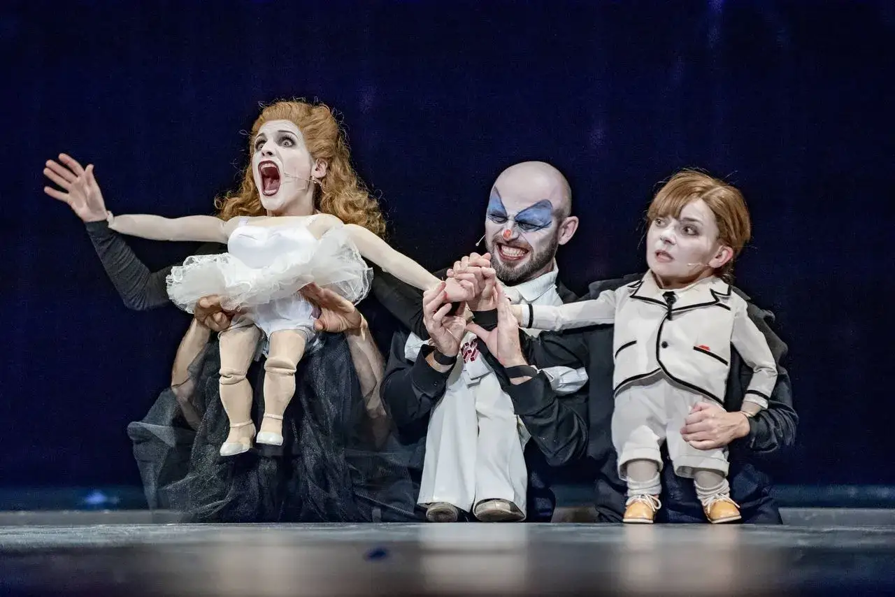 Na dużej scenie Teatru Capitol aktorzy-lalkarze ożywiają kukły. W centrum klaun, po bokach dwie postacie w baletowych strojach.