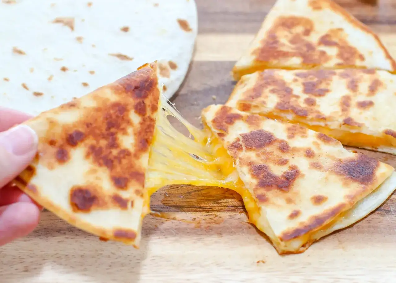 En hand drar isär en gyllene, ostig quesadilla. Perfekt för ett snabbt quesadillas recept.