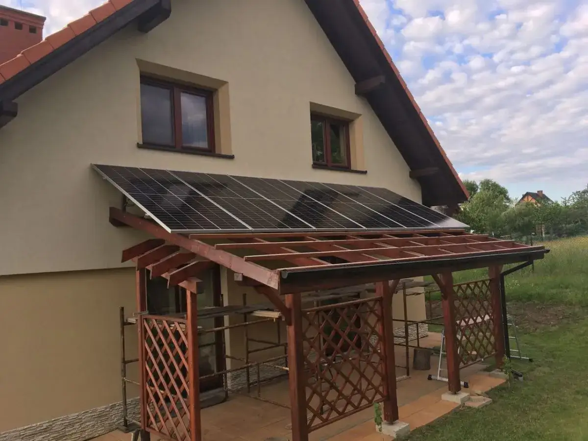 Panele fotowoltaiczne zamontowane nad drewnianą wiatą tarasową, tworząc ekologiczne rozwiązanie.