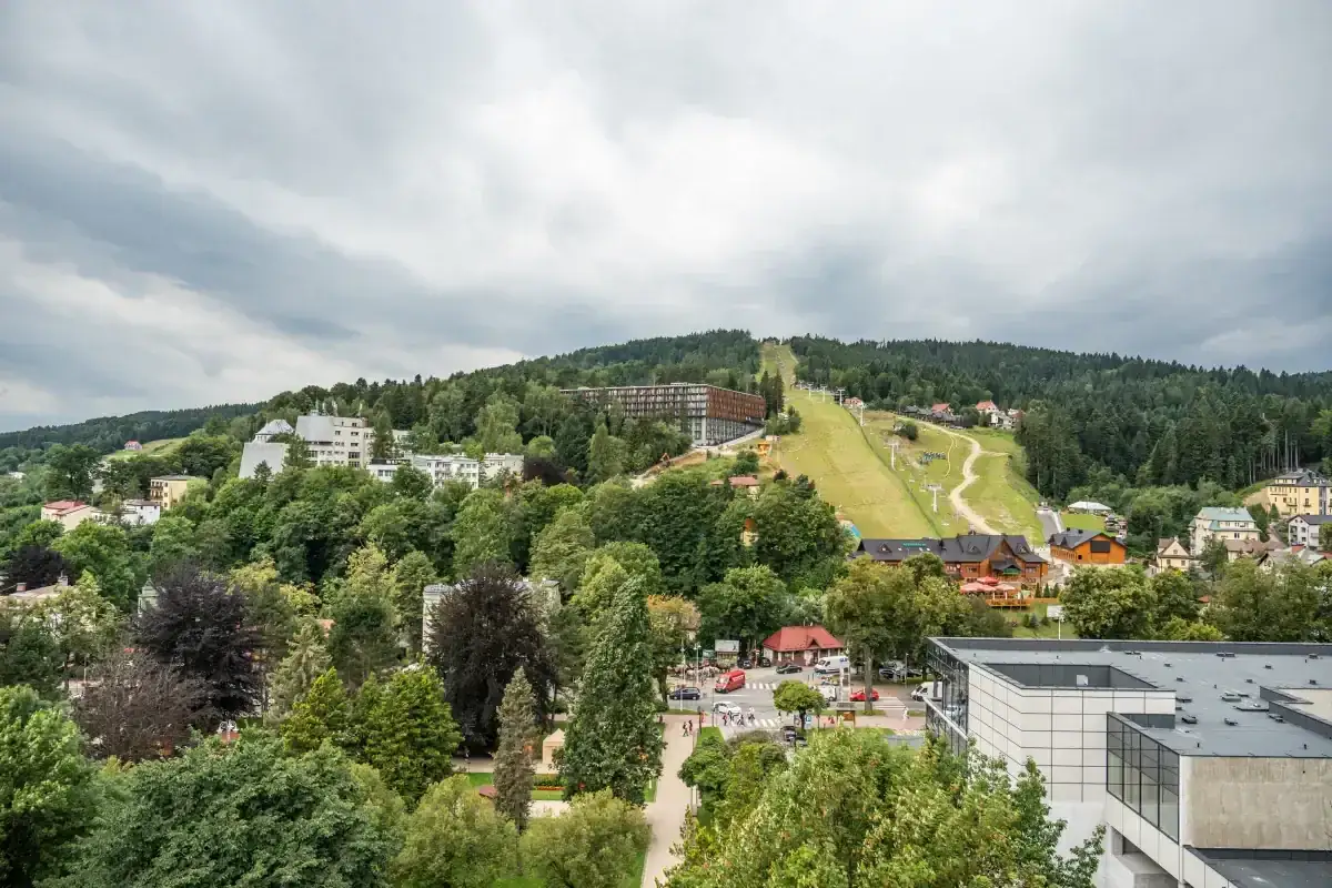 Widok na Krynicę-Zdrój z trasą narciarską i budynkami. Sprawdź sanatorium Krynica Zdrój cennik dla swojej wizyty.