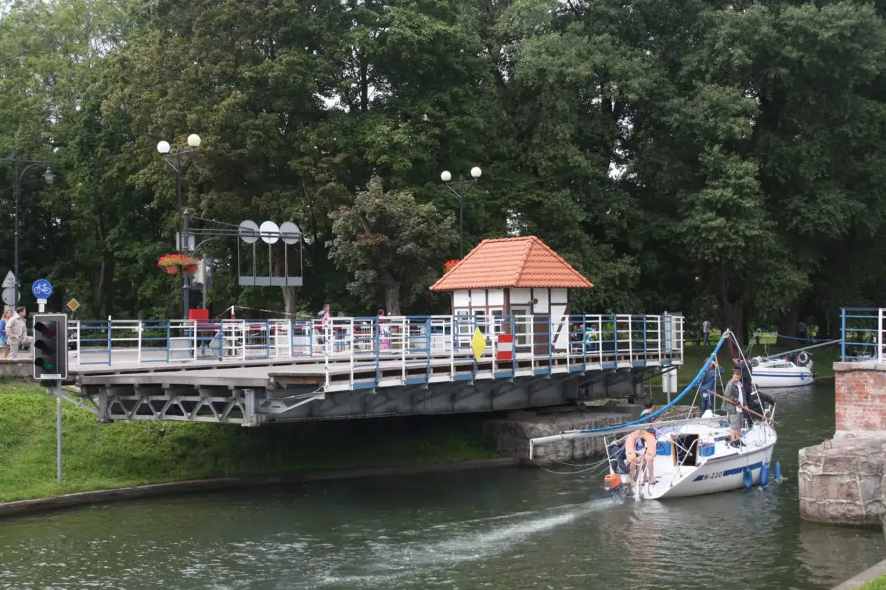 Podniesiony most zwodzony na Mazurach, pod którym przepływa żaglówka. Nietypowe atrakcje Mazury to także takie widoki.