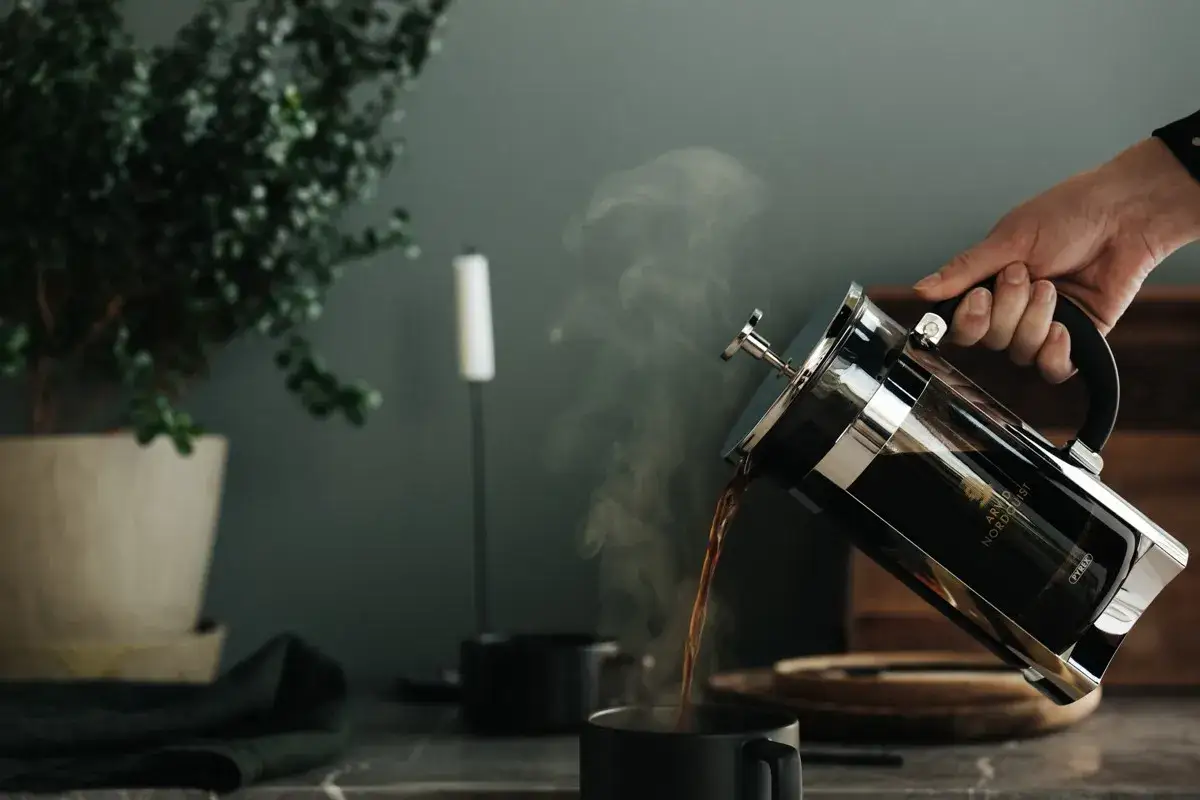En hand h&auml;ller upp &aring;ngande kaffe ur en presskanna. Perfekt presskaffe tid.