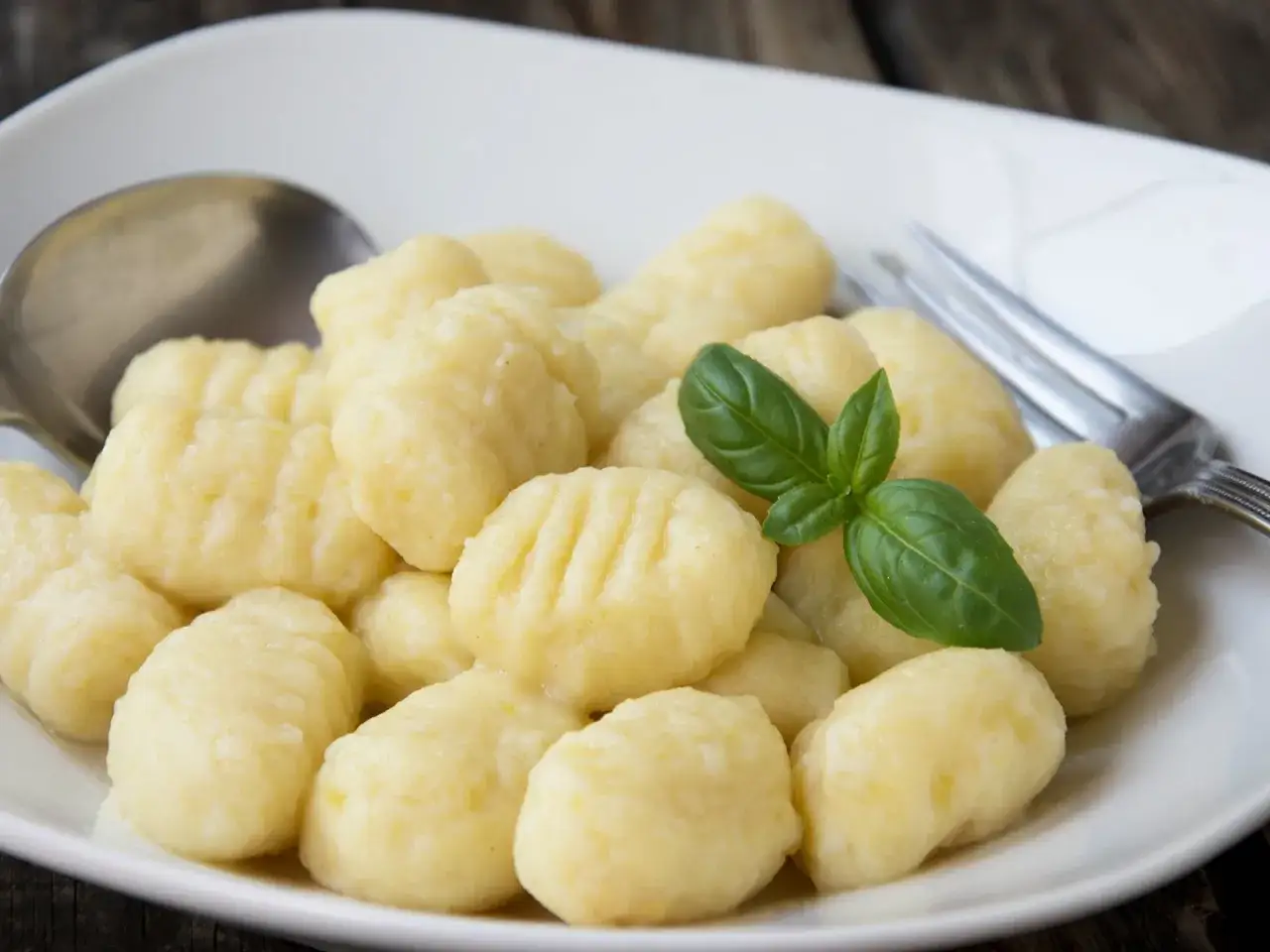 Ein Teller mit köstlichen, **italienischen Gnocchi**, garniert mit frischem Basilikum. Daneben liegen Löffel und Gabel.