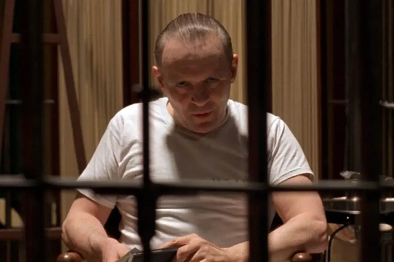 Anthony Hopkins w białej koszulce, siedzący za kratami. Ikoniczna postać z filmów, budząca grozę.