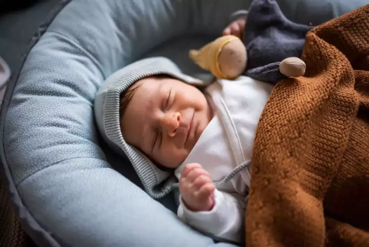 Ein Neugeborenes schläft friedlich in einer Nestchen. Es ist in eine weiche Decke gehüllt, die ihm Geborgenheit gibt, während es seinen Wachstumsschub Baby durchläuft.