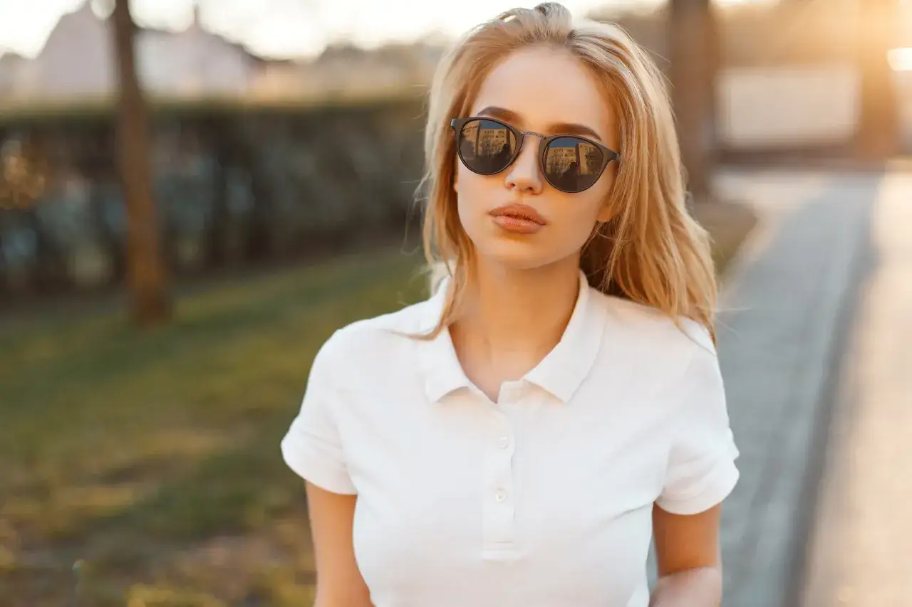 Blondynka w okularach przeciwsłonecznych i białej koszulce polo. Stylowa stylizacja, jak nosić koszulka polo damska na co dzień.