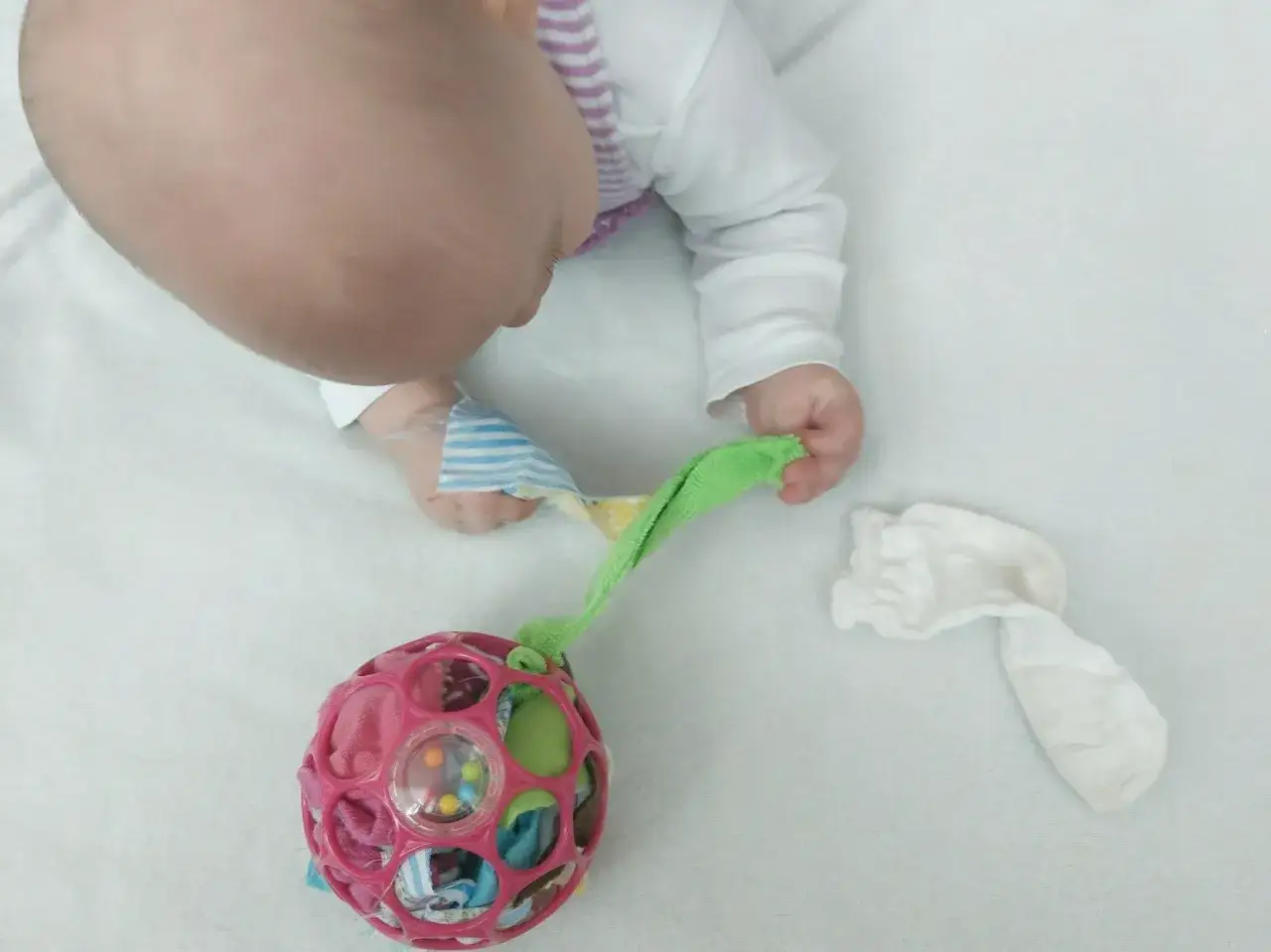 Baby spielt mit selbstgemachtem Spielzeug: bunte Kugel mit Stoffresten und eine weiße Socke. Perfekt zum spielzeug selber machen 1 jahr.