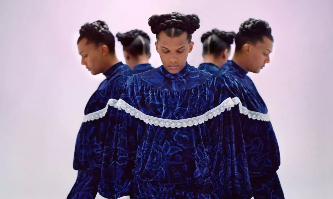 Mehrere Versionen eines Mannes in einem blauen, geblümten Samtkleid mit Zierleisten. Die Kleidung erinnert an die Ästhetik von