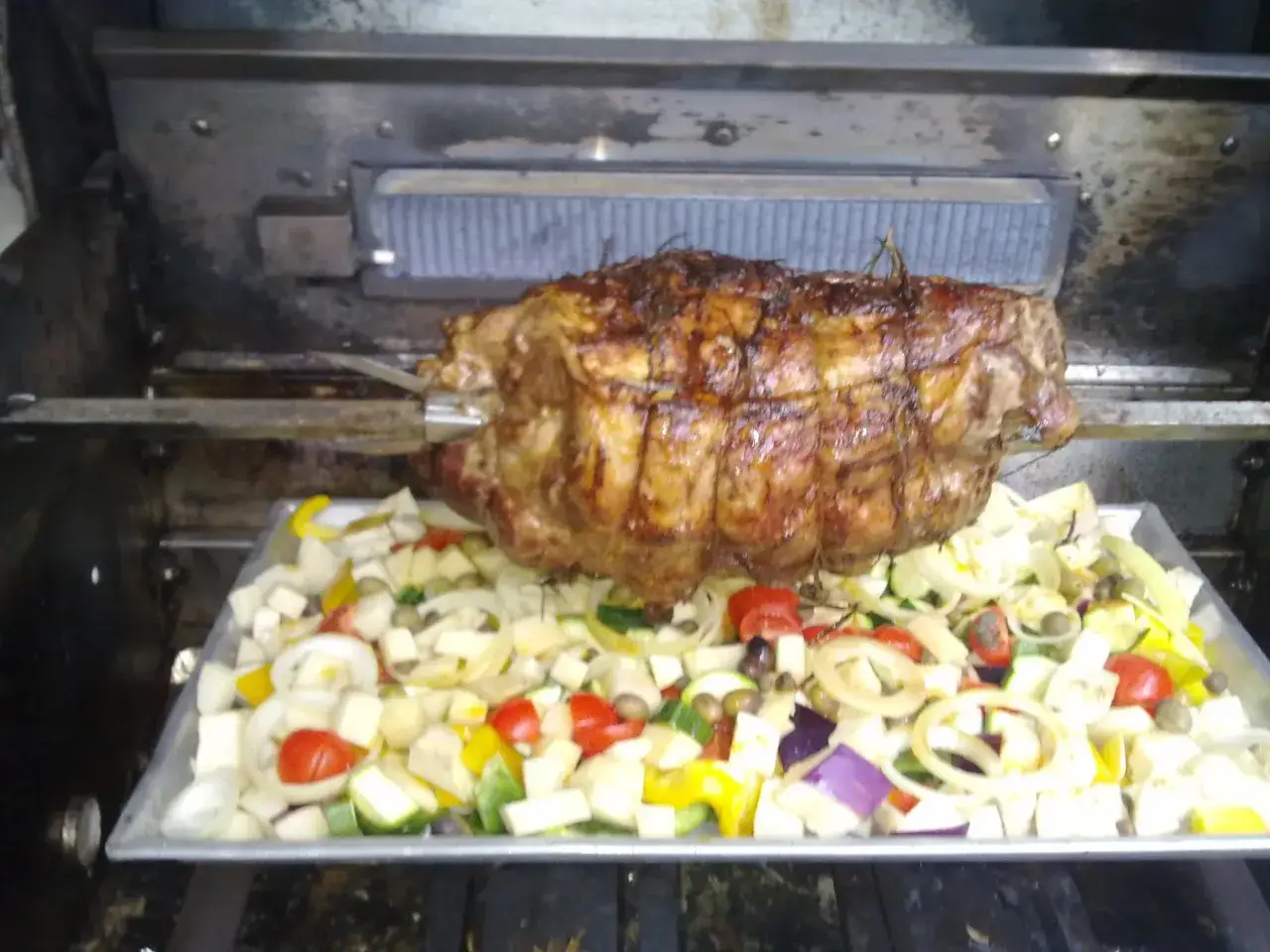 Coppa di maiale allo spiedo dorata e succulenta, circondata da verdure miste tagliate a cubetti: pomodori, zucchine, cipolle, peperoni e olive.