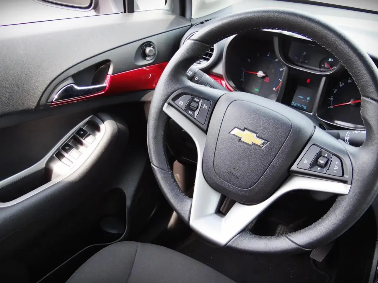 Wnętrze Chevrolet Orlando 1.8 benzyna: kierownica, panel drzwi z przyciskami, czerwone wstawki ozdobne.
