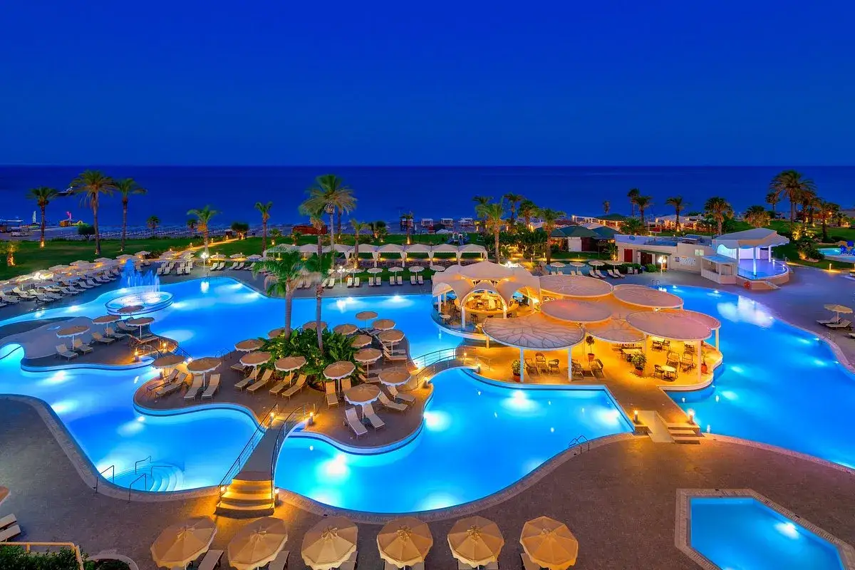Ein beleuchteter Poolbereich mit Palmen und Liegest&uuml;hlen am Abend. Das Lindos Princess Beach Hotel l&auml;dt zum Entspannen ein.