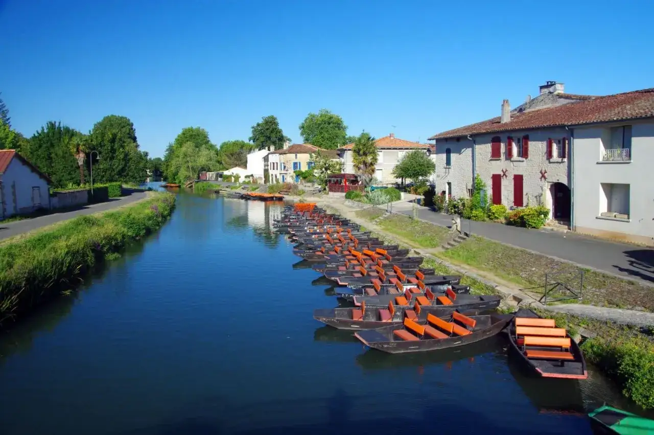 Des barques alignées sur un canal bordé de maisons, idéal pour une exploration en camping-car du Marais Poitevin.